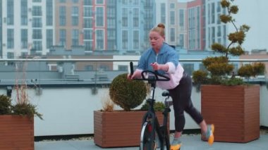 Atletik kız ev çatısı üzerinde bisiklet sürme egzersizleri yapıyor.