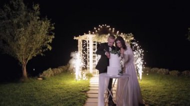 Yeni evliler düğün pastasını kesiyor, güzel gelin ve damat tatlıyı dışarıda bıçakla kesiyor.