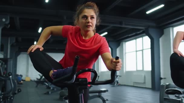Группа улыбающихся друзей женские занятия физкультурой, тренировки, растяжка на стационарном велосипеде в тренажерном зале — стоковое видео