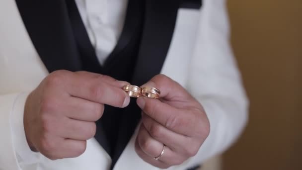 Groom in white jacket holding wedding rings on palm of his hand, man touches the rings, slow motion — Stockvideo