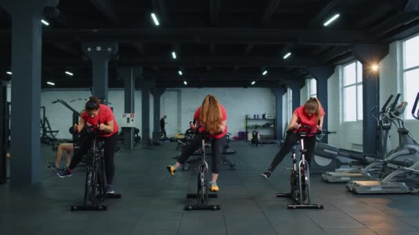 Skupinové atletické dívky provádějící aerobní jízdní trénink na kole stacionární kolo v tělocvičně — Stock video