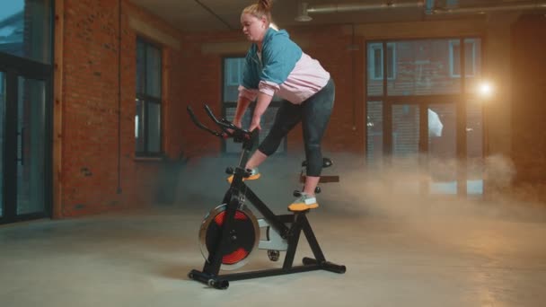 Αθλητική γυναίκα ιππασία σε περιστροφή στατικό ποδήλατο προπόνηση ρουτίνας στο γυμναστήριο ομίχλη, απώλεια βάρους σε εσωτερικούς χώρους — Αρχείο Βίντεο