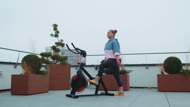 Healthy caucasian woman exercising workout on stationary cycling machine bike on house rooftop gym — Stock Video