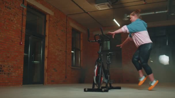 Femeia atletică face rutina de antrenament cu sfoară pe bicicleta staționară în sala de sport, exerciții de întindere — Videoclip de stoc