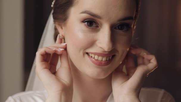 Bruid in boudoir jurk trekt oorbellen, bruiloft ochtend voorbereidingen, vrouw in nachtjapon en sluier — Stockvideo