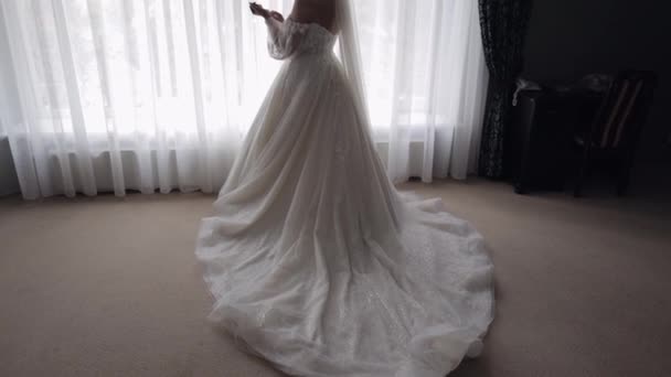 Novia sonriente en vestido blanco que se queda en el dormitorio de casa mirando hacia los lados, preparativos de boda en el hotel — Vídeo de stock