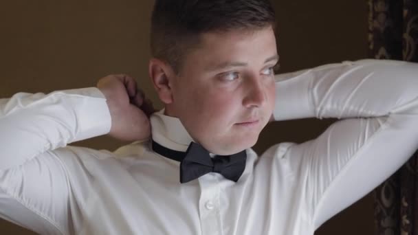 El novio ajusta la corbata de lazo, preparándose para ir a la novia, hombre de negocios con camisa blanca, día de la boda — Vídeo de stock