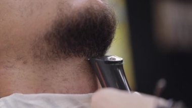 Berber sakal keserken elektrikli makina kullanır, berber dükkanında seyis müşterisine saç tıraşı yapar.