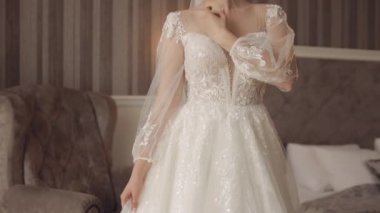 Beyaz elbiseli, gülümseyen gelin, yatak odasında kalıyor ve oteldeki düğün hazırlıklarına bakıyor.