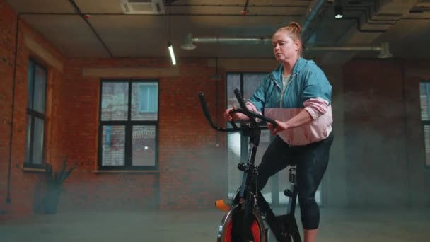 Vrouw voert aeroob uithoudingsvermogen training workout cardio routine op de simulatoren, cyclus training — Stockvideo