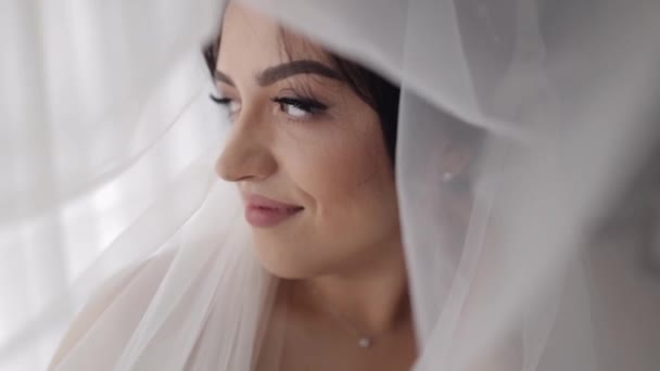 Улыбающаяся невеста в белом платье, сидящая дома в спальне, смотрит на подготовку к свадьбе в отеле — стоковое видео