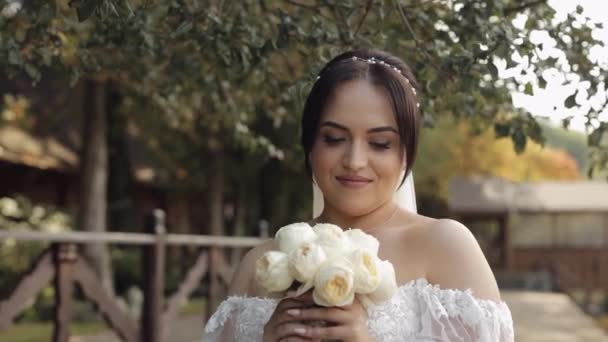 Schöne stilvolle Braut in weißem Brautkleid und Schleier hält Brautstrauß in Händen im Park — Stockvideo