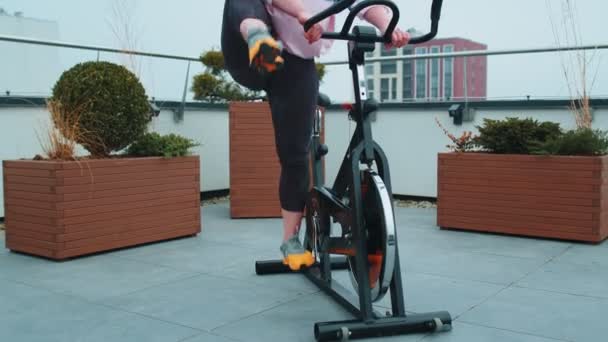 Athletic woman riding on spinning stationary bike training routine on house rooftop, weight loss — Stock Video