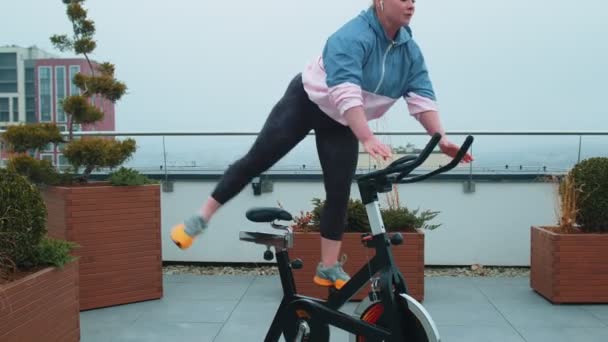 Αθλητική γυναίκα ιππασία για περιστροφή στατικό ποδήλατο προπόνηση ρουτίνας στην οροφή του σπιτιού, απώλεια βάρους — Αρχείο Βίντεο