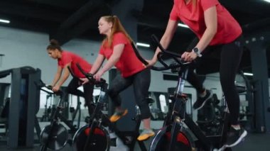 Bir grup gülümseyen arkadaş. Modern spor salonunda kadın sınıfı spor yapıyor, antrenman yapıyor, bisiklete biniyor.