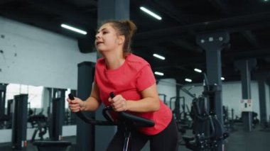 Spor salonunda bisiklete binen atletik genç bir kadın spor salonunda spor yapıyor, evde kilo kaybediyor.