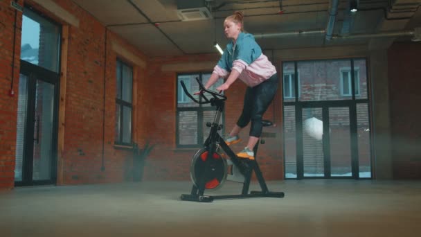 Здоровая белая женщина, занимающаяся спортом на стационарном велосипеде в тренажерном зале, Slow Motion — стоковое видео