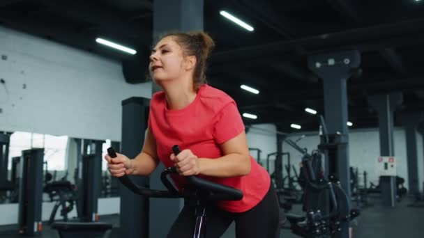 Sportos fiatal nő lovaglás forgó álló kerékpár edzés rutin tornaterem, fogyás beltéri — Stock videók
