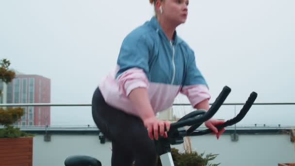Femme athlétique chevauchant sur la rotation de routine d'entraînement de vélo stationnaire sur le toit de la maison, perte de poids — Video