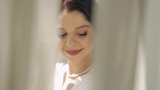 Νύφη σε μπουντουάρ φόρεμα κοντά στο παράθυρο, γαμήλιες πρωινές προετοιμασίες, γυναίκα με νυχτικό και πέπλο — Αρχείο Βίντεο