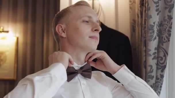 Groom man adjusts bow tie, preparing to go to the bride, businessman in white shirt, wedding day — Stockvideo