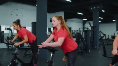 Sağlıklı bir beyaz kadın grubu spor salonunda sabit bisiklet üzerinde egzersiz yapıyor.