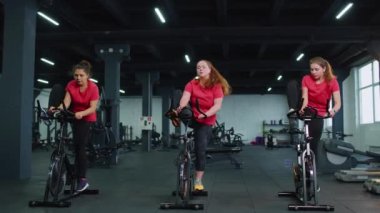 Spor salonunda bisiklet çevirme antrenmanına katılan atletik kadın grubu, içeride kilo kaybı.