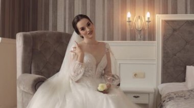 Beyaz elbiseli gelin yatak odasında sandalyede oturuyor. Damat için düğün buketi hazırlıyor.