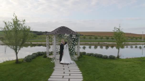 Frischvermählte, Bräutigam, Braut Umarmung, Umarmungen, Küssen, Hochzeitszeremonie, Bogen mit Blumen — Stockvideo