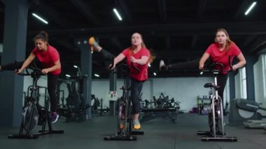 Sağlıklı bir beyaz kadın grubu spor salonunda sabit bisiklet üzerinde egzersiz yapıyor.