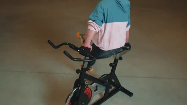Atletická dívka, aby akrobatický trik na kole cvičení na stacionární cyklistické stroje uvnitř — Stock video