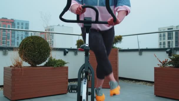 Спортсменка виконує аеробні вправи з підготовки їзди на велосипеді стаціонарний велосипед на даху будинку — стокове відео