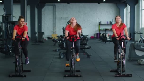 Группа улыбающихся друзей женские классы упражнения, тренировки, спиннинг на стационарном велосипеде в современном тренажерном зале — стоковое видео