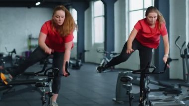 Sağlıklı bir beyaz kadın grubu spor salonunda sabit bisiklet üzerinde egzersiz yapıyor.