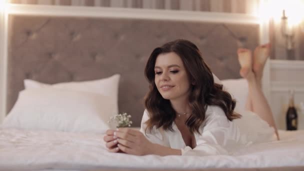 Linda mulher noiva elegante em vestido de noite sob véu com buquê, deite-se na cama no quarto em casa — Vídeo de Stock