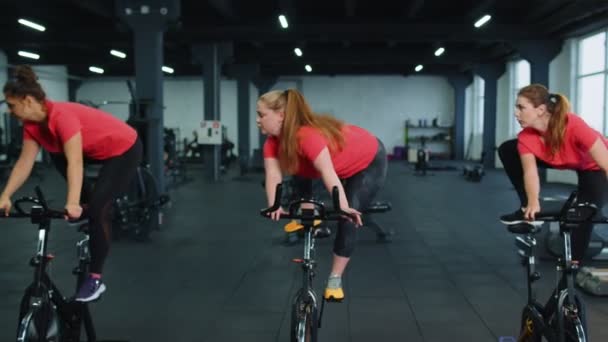 Group athletic girls performing aerobic riding training exercises on cycling stationary bike in gym — Stock Video