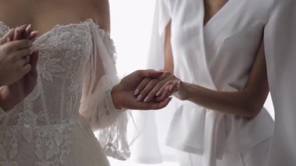 Наречені подружки подружки наречених в сукні допомагають жінці одягатися на весільну сукню, тримаючись за руку — стокове відео