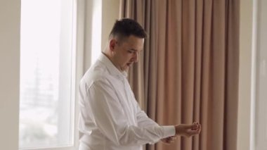 Handsome groom man dresses in wedding morning and fixes his cufflink buttons on a white shirt sleeve