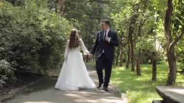Sevgili yeni evliler, beyaz gelin damat parkta yürüyor, el ele tutuşuyorlar, düğün çifti ailesi.