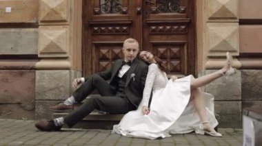 Newlyweds love, caucasian groom with bride sitting, embracing, hugs in city street, wedding couple