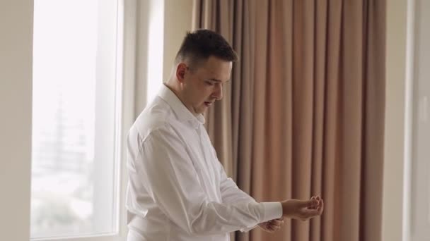 Handsome groom man dresses in wedding morning and fixes his cufflink buttons on a white shirt sleeve — Stockvideo