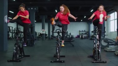 Sağlıklı bir beyaz kadın grubu spor salonunda sabit bisiklet üzerinde egzersiz yapıyor.