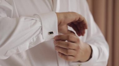 Handsome groom man dresses in wedding morning and fixes his cufflink buttons on a white shirt sleeve