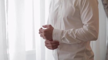 Yakışıklı damat düğün sabahı giyiniyor ve düğmelerini beyaz gömleğin koluna takıyor.