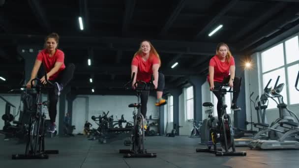 Здоровая кавказская группа женщин, занимающихся спортом на стационарных велосипедах в тренажерном зале — стоковое видео
