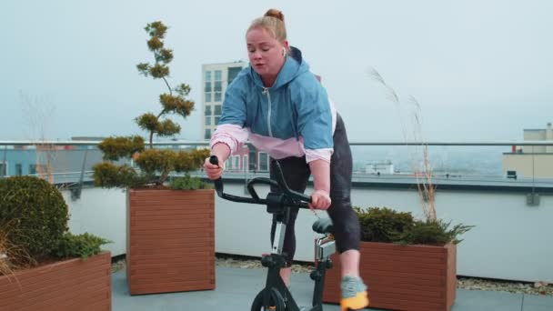 Femme caucasienne en bonne santé faisant de l'exercice sur une machine à vélo stationnaire sur le toit de la maison gymnase — Video