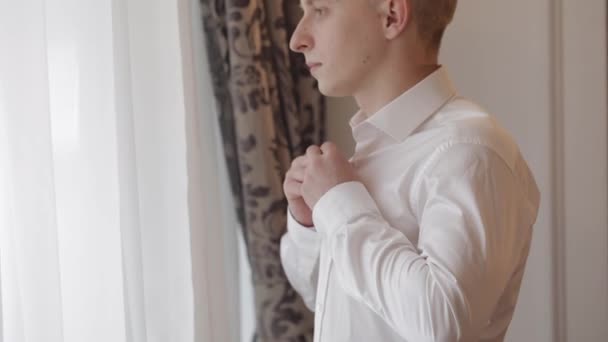 Stylowy mężczyzna w kurtce zapina guziki, zapinając białą koszulę przygotowując się do wyjścia przez okno — Wideo stockowe