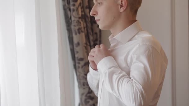 Stylish man in jacket fastens buttons, buttoning white shirt preparing to go out near window — Stock Video