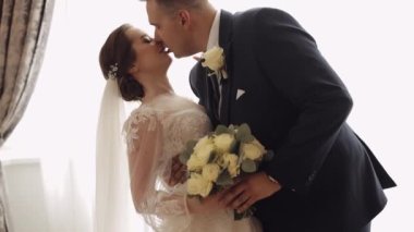 Newlyweds portrait, caucasian groom bride walking, embracing, hugs in living room, wedding couple