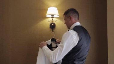 Handsome groom businessman taking and preparing to wear white jacket at home at home living room